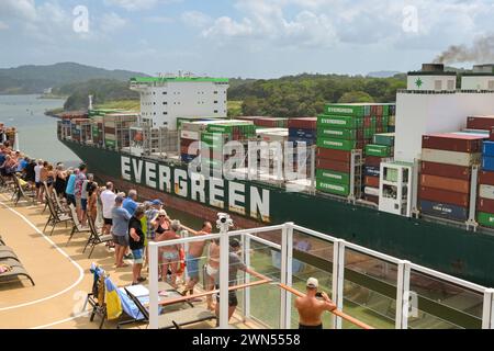 Panamakanal, Panama - 23. Januar 2024: Passagiere auf dem Oberdeck eines Kreuzfahrtschiffs mit Blick auf ein vorbeifahrendes Containerschiff Stockfoto