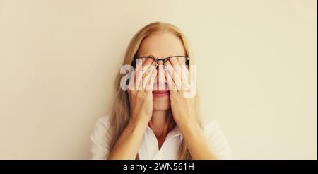 Müde überarbeitete Frau, die sich die Augen reibt und unter Augenanstrengung, trockenem Auge-Syndrom oder Kopfschmerzen leidet Stockfoto