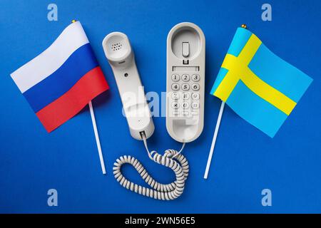 Altes Telefon und zwei Flaggen auf blauem Hintergrund, Konzept zum Thema Telefongespräche zwischen Schweden und Russland Stockfoto