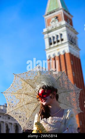 Venedig, VE, Italien - 13. Februar 2024: Hübsches Mädchen mit roter Maske und Lippenstift und edlem Kleid am Markusplatz während des venezianischen Karnevals Stockfoto
