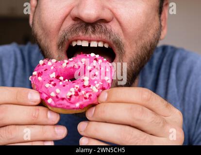 Der Mann isst rosafarbene Donut-Nahaufnahme-Mund. Stockfoto