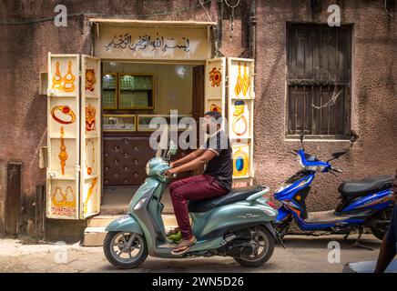 Ein Mann auf einem Motorroller fährt an einem Juweliergeschäft in Stone Town, Sansibar, Tansania vorbei Stockfoto