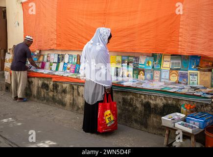 Ein muslimischer Mann und eine muslimische Frau halten an, um sich einen Straßenbuchsstand in Stone Town, Sansibar, Tansania anzuschauen Stockfoto