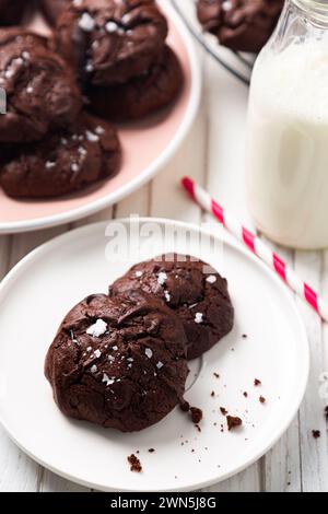 Leckerer Snack mit hausgemachten Brownie-Keksen mit zerbrochenem Oberteil und Salzflocken auf einem Gericht und einer kleinen Flasche Milch Stockfoto