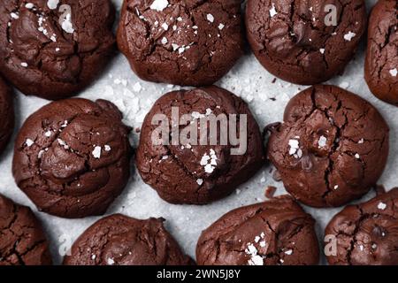 Blick von oben auf hausgemachte Brownie-Kekse mit zerbrochenem Oberteil und Salzflocken auf Backpapier Stockfoto