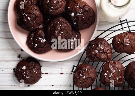 Leckerer Snack mit hausgemachten Brownie-Keksen mit zerbrochenem Oberteil und Salzflocken auf einem rosafarbenen Gericht und einer kleinen Flasche Milch Stockfoto