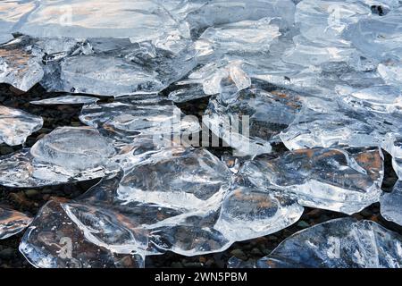 Gefrorenes Eis am Seeufer überschneidet sich, um eine Szene mit Eisreflexen und -Formen zu bilden. Stockfoto