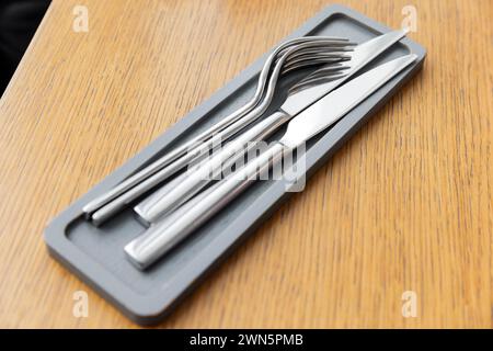 Glänzende Gabeln und Messer aus Edelstahl liegen auf einer kleinen grauen Holzschale auf einem leeren Holztisch Stockfoto