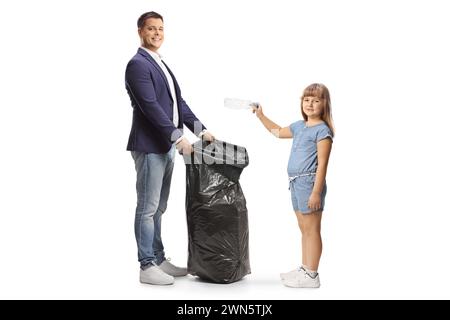 Profilaufnahme eines Mädchens, das eine Plastikflasche in einen schwarzen Abfallbeutel wirft, isoliert auf weißem Hintergrund Stockfoto