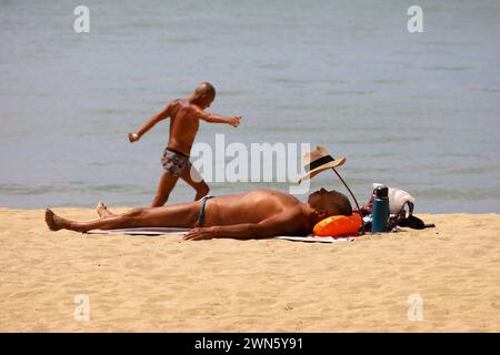 Gebräunter asiatischer Mann in Koffern, der am Sandstrand schläft Stockfoto