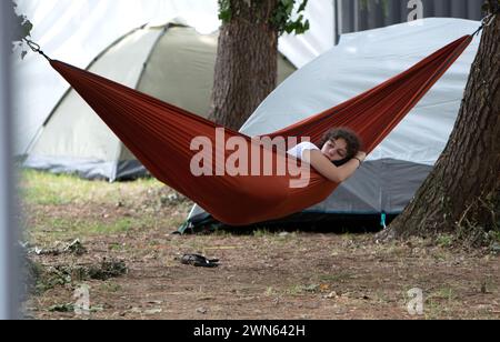 Lockige, brünette Haare, Ruhe. Entspannende Natur. Ein junges Mädchen, das sich entspannt, auf brauner Hängematte. Campingzone. Stockfoto