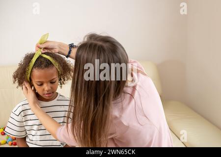 In einem komfortablen Zuhause genießen eine Frau und ihre junge schwarze Tochter eine schöne Zeit, während sie eine spielerische Friseur erleben, die Mutter symbolisiert Stockfoto