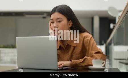 Müde gelangweilte asiatische Geschäftsfrau Mädchen sitzen im Café und arbeiten an Laptop traurig erschöpft chinesisch japanisch koreanisch Dame faule Studentenführerin Stockfoto