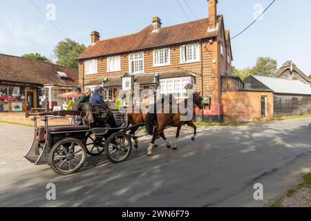 Minstead New Forest Village, zwei ältere Männer auf einem Pferdewagen, die von zwei braunen Pferden an der Trusty Servant Inn, Hampshire, England, UK, 2023 vorbeigezogen wurden Stockfoto
