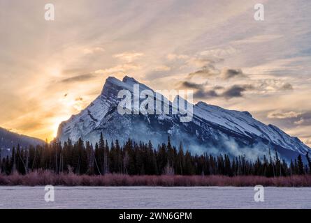 Wintersonnenaufgang über gefrorenen Vermilion-Seen im Banff-Nationalpark mit Mount Rundle im Hintergrund und Kiefernsilhouette entlang des Banff-Nationalparks Stockfoto