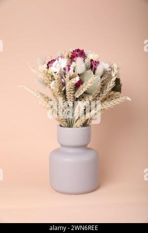 Strauß von schönen trockenen Blumen und Spikelets in Vase auf beigem Hintergrund Stockfoto