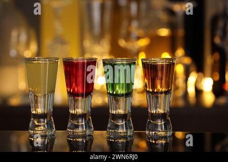 Verschiedene Schützen in Schussgläsern auf Spiegeloberfläche vor verschwommenem Hintergrund. Alkohol trinken Stockfoto