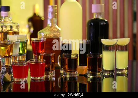 Verschiedene Schützen in Schussgläsern und Flaschen auf Spiegeloberfläche. Alkohol trinken Stockfoto