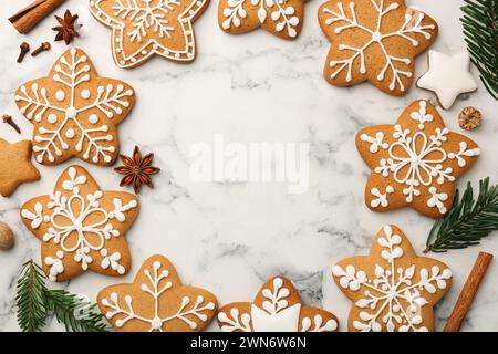 Rahmen aus leckeren sternförmigen Weihnachtsplätzchen mit Glasur, Gewürzen und Tannenzweigen auf weißem Marmortisch, flach gelegt. Leerzeichen für Text Stockfoto