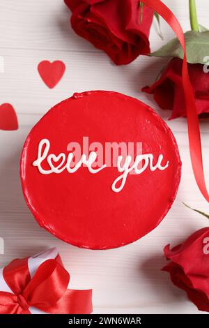 Bento-Kuchen mit Text Love You, Geschenkbox, Rosen und Papierherzen auf weißem Holztisch, flacher Lay. St. Valentinstag-Überraschung Stockfoto