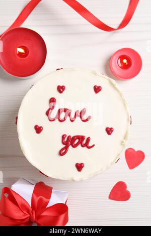 Bento-Kuchen mit Text Love You, Geschenkbox, Kerzen und Papierherzen auf weißem Holztisch, flacher Lay. St. Valentinstag-Überraschung Stockfoto