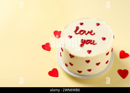 Bento Kuchen mit Text Love You und Papierherzen auf beigem Tisch, Platz für Text. St. Valentinstag-Überraschung Stockfoto