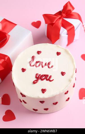 Bento Kuchen mit Text Love You, Geschenkboxen und Papierherzen auf rosa Tisch. St. Valentinstag-Überraschung Stockfoto