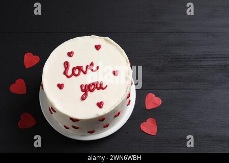 Bento Kuchen mit Text Love You und Papierherzen auf schwarzem Holztisch, Platz für Text. St. Valentinstag-Überraschung Stockfoto