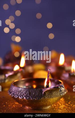 Diwali-Feier. Diya-Lampe auf glänzend goldenem Tisch gegen verschwommenes Licht, Nahaufnahme Stockfoto