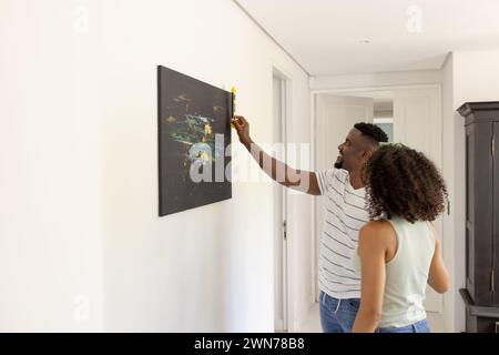 Birassisches afroamerikanisches Paar hängt zu Hause ein Gemälde mit Kopierraum auf Stockfoto