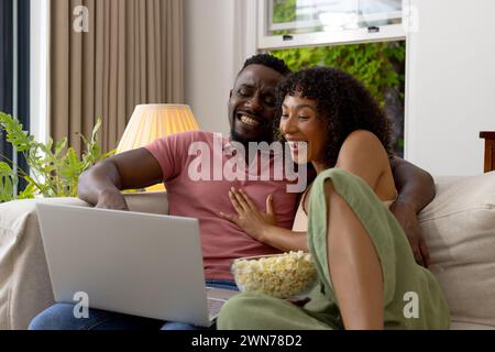 Birassisches afroamerikanisches Paar lacht, während er zu Hause einen Laptop benutzt Stockfoto