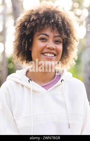 Die junge birassische Frau lächelt hell auf einer Wanderung und trägt einen lässigen weißen Hoodie Stockfoto