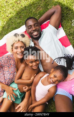 Die vielfältige Familie genießt einen sonnigen Tag im Freien und liegt auf einer bunten Decke Stockfoto