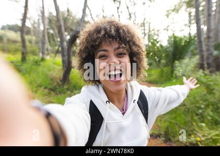 Eine junge birassische Frau mit lockigen Haaren macht ein Selfie, die Arme sind vor Freude auf einer Wanderung ausgestreckt Stockfoto