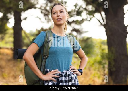 Junge kaukasische Frau mit Rucksack steht selbstbewusst draußen auf einer Wanderung Stockfoto