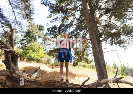 Die junge kaukasische Frau genießt die Natur an einem sonnigen Tag auf einer Wanderung, die Arme in einem Wald gestreckt Stockfoto