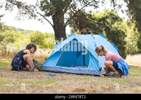 Eine junge Frau mit birassischen und kaukasischen Frauen haben draußen ein blaues Zelt aufgebaut Stockfoto