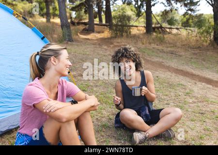 Junge kaukasische Frau und birassische Frau unterhalten sich neben einem Zelt Stockfoto