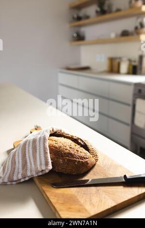 Sonnendurchflutete Küchenszene mit Brot an Bord unter Handtuch, das Wärme weckt. Stockfoto