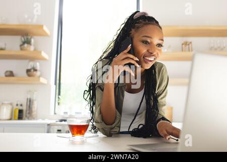 Die junge afroamerikanische Frau spricht am Telefon, während sie einen Laptop benutzt Stockfoto