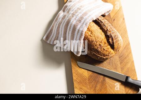 Ein frisch gebackener Brotlaib liegt auf einem hölzernen Schneidebrett neben einem Messer, mit Kopierraum Stockfoto