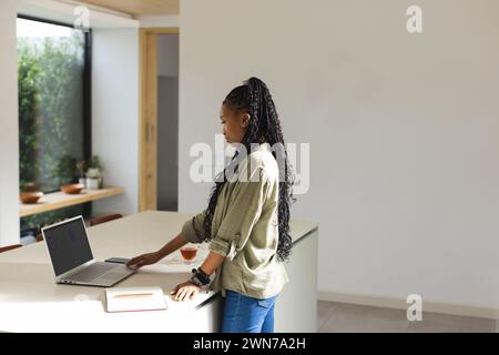 Eine junge Afroamerikanerin steht an einem weißen Tisch mit Laptop und Kopierraum Stockfoto