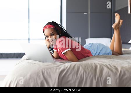 Eine junge Afroamerikanerin liegt auf ihrem Bauch mit einem Laptop auf einem Bett Stockfoto