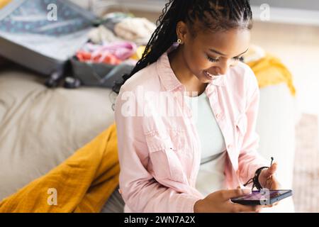 Eine junge Afroamerikanerin lächelt, während sie ihr Smartphone benutzt Stockfoto