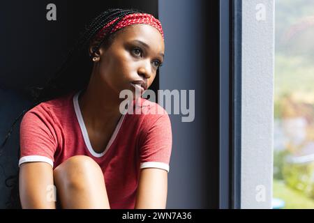 Eine junge Afroamerikanerin schaut aus dem Fenster, tief in Gedanken, mit Kopierraum Stockfoto