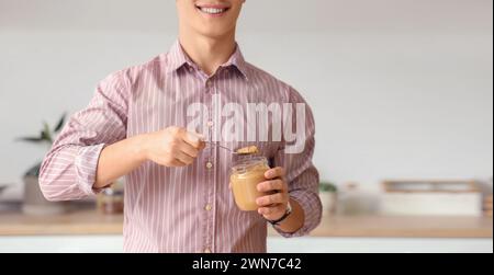 Glücklicher junger Mann mit leckerer Nussbutter in der Küche Stockfoto