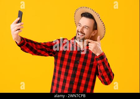 Ein gutaussehender Mann mit Handy, der Selfie auf gelbem Hintergrund macht. Festa Junina (Juni-Festival) Stockfoto