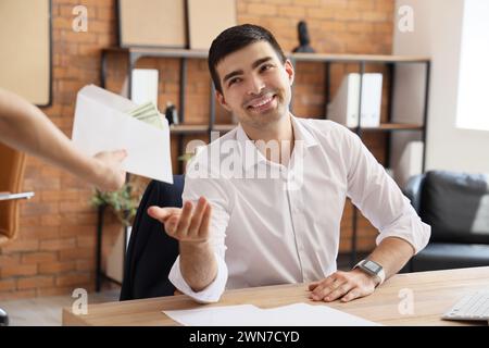 Junger Geschäftsmann, der im Büro einen Umschlag mit Geld nimmt Stockfoto