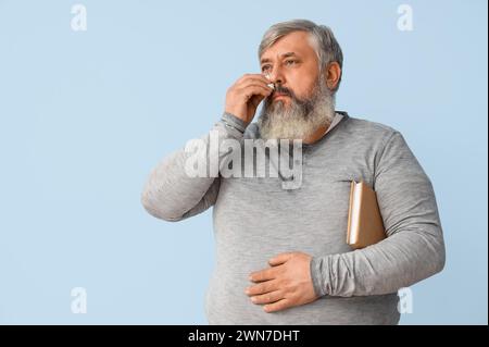 Porträt eines traurigen älteren Mannes mit Büchern, die Augen auf hellblauem Hintergrund abwischen Stockfoto