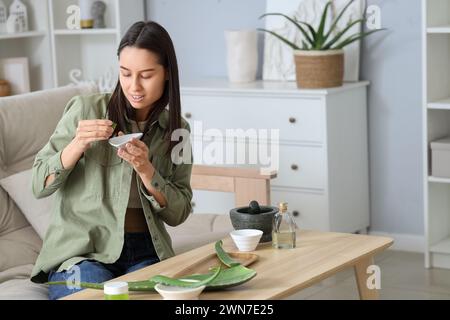 Schöne junge Frau, die Aloe Vera Gel im Wohnzimmer herstellt Stockfoto